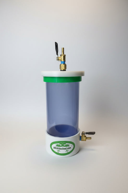 A clear, cylindrical vacuum chamber, white top, featuring brass fittings and valves.