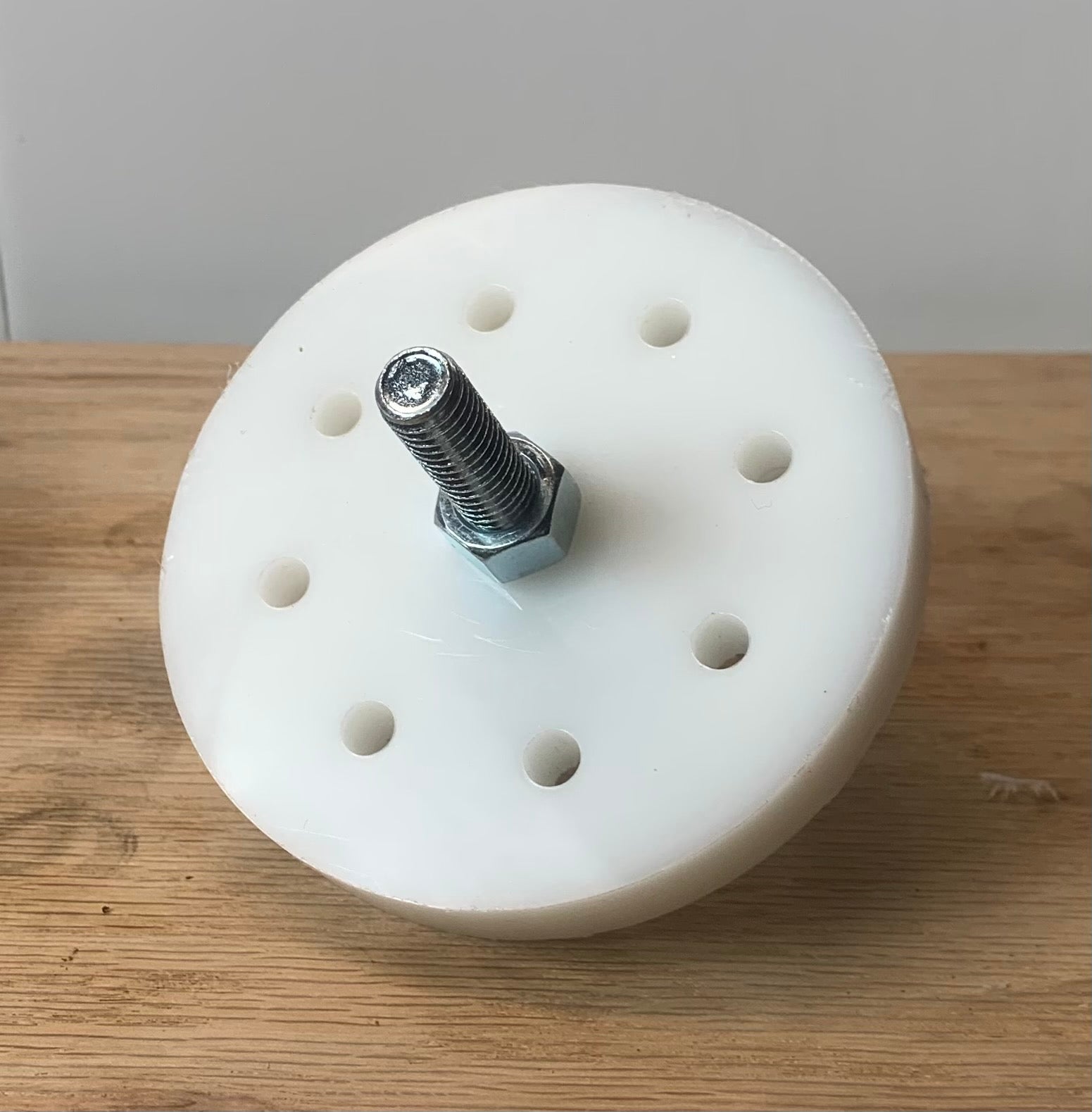 A white circular weight plug with multiple holes and a central bolt, placed on a wooden surface.