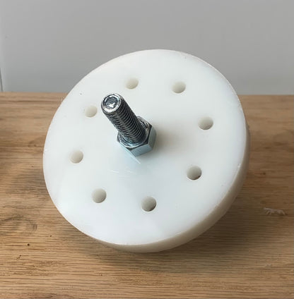 A white circular weight plug with multiple holes and a central bolt, placed on a wooden surface.